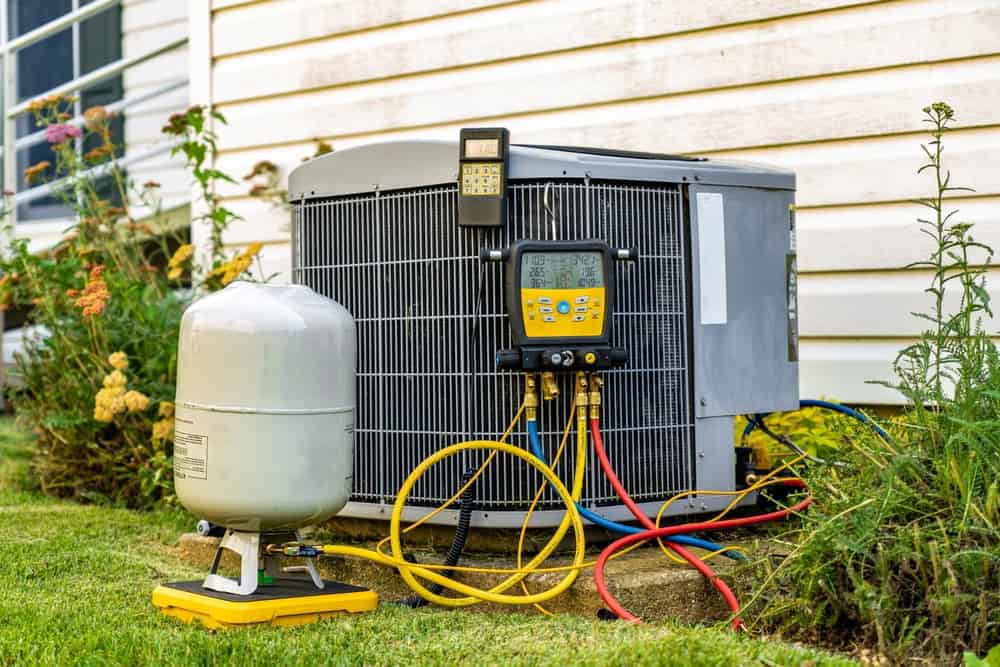  Outdoor AC condenser unit connected to refrigerant tank and digital manifold gauge for diagnostic and maintenance checks.