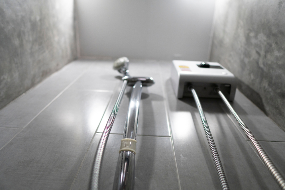Wall-mounted tankless water heater with attached shower head in a tiled bathroom with minimalist concrete walls.